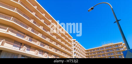 Abstract of sunlit building balcony line uniformity, street lamp in daytime.  Hotel exterior & facade with balconies.  Street level view looking up. Stock Photo