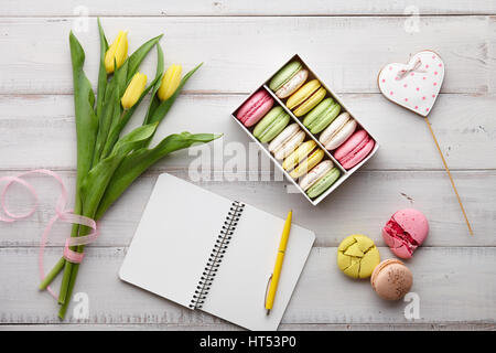 Copybook, tulips and macarons on wooden table Stock Photo