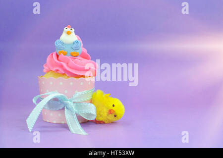 Happy Easter pink, yellow and blue cupcakes with cute chicken decorations on purple background and with copy space, with faded lens flare filter. Stock Photo