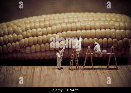 Miniature painters coloring corn on the cob. Macro photo Stock Photo
