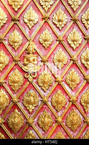 Closed-up vintage golden concrete stucco design of native traditional Thai mural art on the red Wall Stock Photo