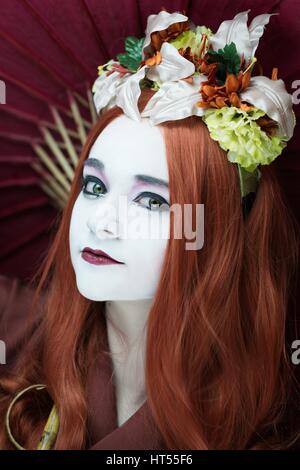 Woman dressed as a Geisha girl with parasol and floral garland in her hair Stock Photo