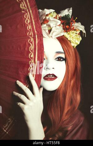 Woman dressed as a Geisha girl with parasol and floral garland in her hair Stock Photo