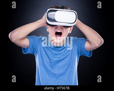 Amazed teen boy screaming, wearing virtual reality goggles watching movies or playing video games. Surprised teenager looking in VR glasses and shouti Stock Photo