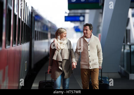 Beautiful senior couple on trainstation pulling a trolley luggage. Stock Photo