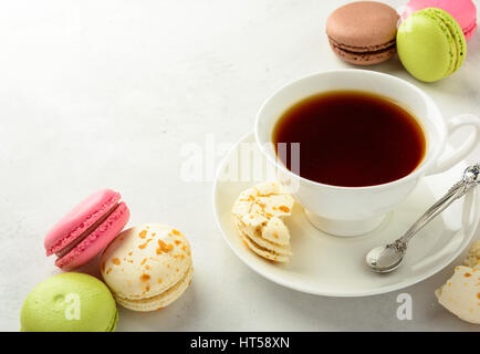 Cup of black tea with tasty almond cookies, rich in vitamins, minerals, varicolored macaroons and flowers on a white background in light key. Top view Stock Photo