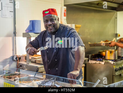 Afro- Caribbean Chef leaning over the serving counter in his kitchen. Stock Photo