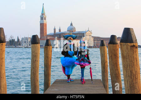 Two people in costumes on a boat landing outside San Giorgio Maggiore during the Carnival of Venice, Italy Stock Photo