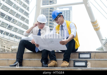 Two asian architects discussing about new project with paperwork at step of business walk way area in the city. Stock Photo