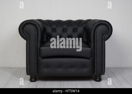 Black leather armchair on white wooden floor near white textured wall Stock Photo