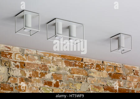 Light stylish lamps on the ceiling over the brick wall. They drop shadows on the ceiling. Closeup. Horizontal. Stock Photo