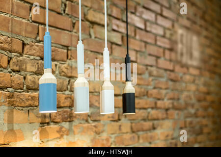 Four glowing hanging multi-colored lamps in a loft style on the brick wall background. Closeup. Horizontal. Stock Photo