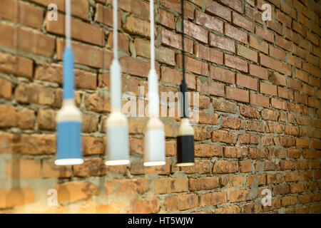 Low aperture photo of the glowing hanging multi-colored lamps in a loft style on the brick wall background. Closeup. Horizontal. Stock Photo