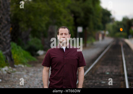 Man with a serious stern expression standing on the railroad tracks alone. Stock Photo