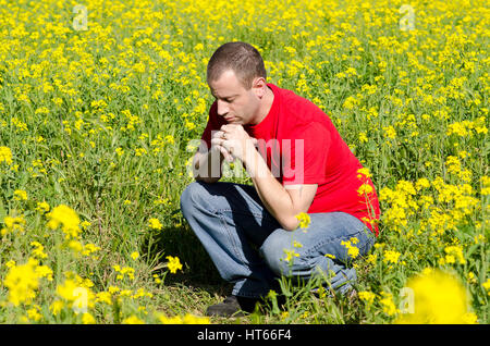 Man in a red shirt praying alone in a field of yellow flowers. Stock Photo