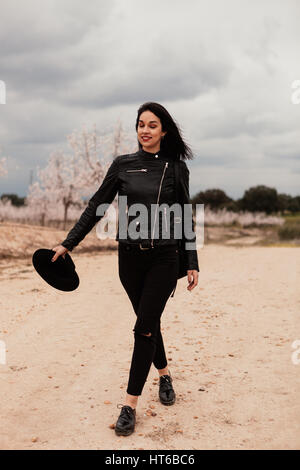 Brunette woman with leather jacket walking on a path with flowered almond trees Stock Photo