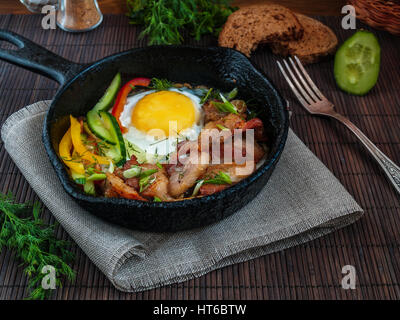 Scrambled eggs with bacon and vegetables custard bread in a pan on the Llano chugonnoy napkin on a table on a bamboo stand Stock Photo