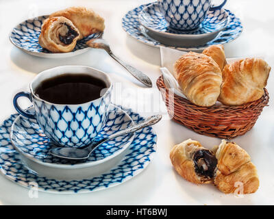 Croissants in a basket on a napkin for breakfast on a table with tea cups with spoons saucers Stock Photo