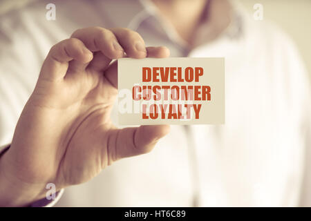 Closeup on businessman holding a card with text DEVELOP CUSTOMER LOYALTY, business concept image with soft focus background and vintage tone Stock Photo