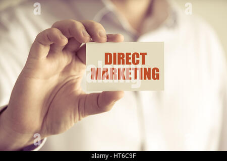 Closeup on businessman holding a card with text DIRECT MARKETING, business concept image with soft focus background and vintage tone Stock Photo