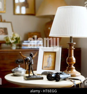 'Side table with table lamp, female figurine and binoculars.' Stock Photo
