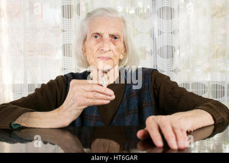 Old grandma smoking a cigarette at home Stock Photo