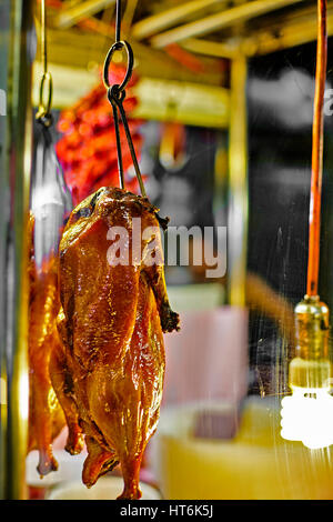 Chinese Roast Duck street food hanging on hook behind faded glass at night in downtown Chinatown Stock Photo