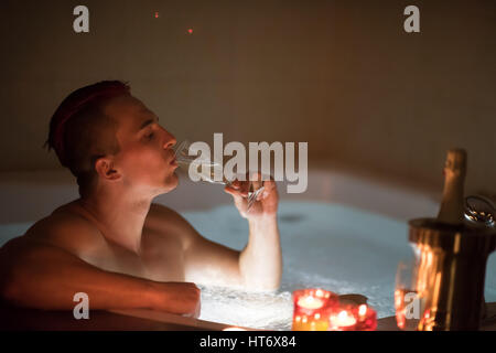 young handsome man enjoys relaxing in the jacuzzi with candles and champagne at luxury resort spa Stock Photo