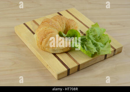 Sandwich preparation of sliced croissant and lettuce on cutting board Stock Photo