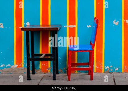 A wooden table with a cowhide chair are seen in front of the brightly paited facade of a colonial house in Jardín, a coffee village in Colombia. Stock Photo