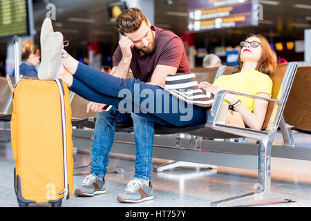 Young couple sleeping on the chairs at the waiting room of the airport. Long waiting for the airplane Stock Photo