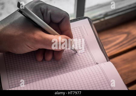 Close up view of men's left Hand With pen drawing smile in notepad. Personal Organizer Stock Photo