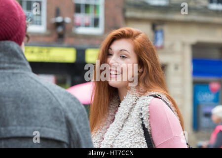 A happy female student smiles as she stands amongst her friends outdoors. They are taking a break from university in the city centre. Stock Photo