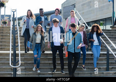 A group of young teenage students smile as they walk through the city on a break from university. They are carrying their books and digital tablets. Stock Photo