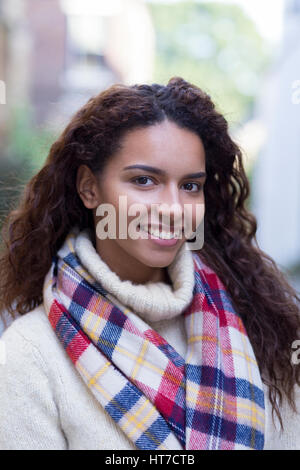 A happy young female student smiles at the camera. She is wearing a cream jumper and checked scarf. Stock Photo