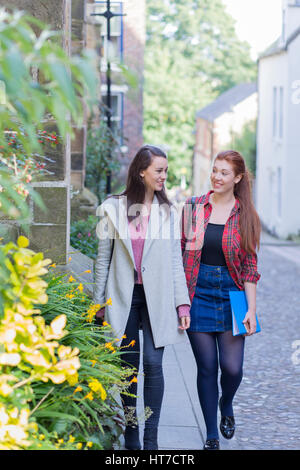 Two happy female students smile as they walk through the streets on a break. They are carrying bags and work folders. Stock Photo
