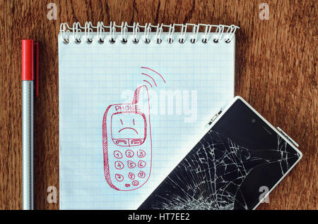Freehand drawing of old phone in notebook. Smartphone with broken screen on wooden table. Dream, visualization desire, need a new phone concept Stock Photo