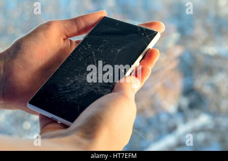 White Smartphone with broken screen in human hands on blured nature background Stock Photo