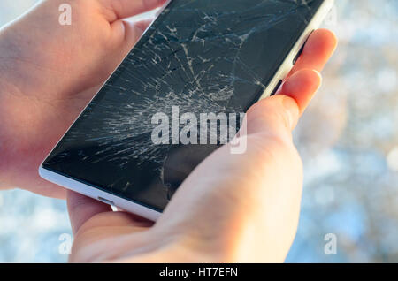 White Smartphone with broken screen in human hands on blured nature background Stock Photo