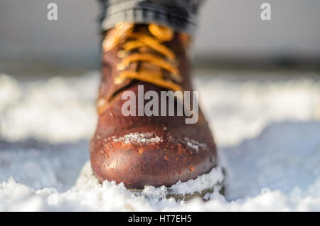 Snow melts on brown winter boots. Brown leather shoes in the snow. Shallow depth of field. Legs in the warmth concept. Stock Photo