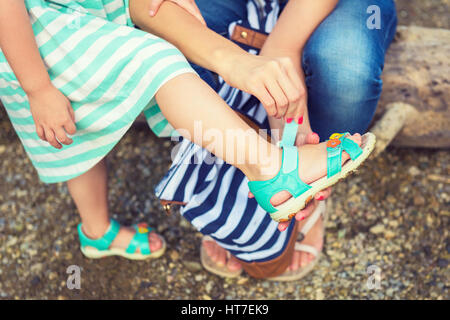 Mother helping her daugter to put on summer sandals Stock Photo