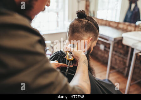 Man getting haircut by barber at salon. Hairdresser cutting hair of client with hair trimmer machine. Stock Photo