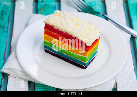 Rainbow cake on a white plate. Wooden background. Stock Photo