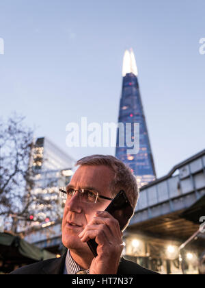City businessman outdoors serious talking on his smartphone iPhone at dusk with 'The Shard' tower in background London SE1 Stock Photo