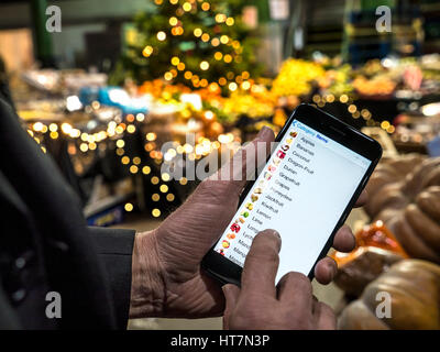 BOROUGH MARKET CHRISTMAS SMART SHOPPING Hand holding smartphone iPhone with interactive fruit and vegetable prompts on-screen Borough Market London UK Stock Photo