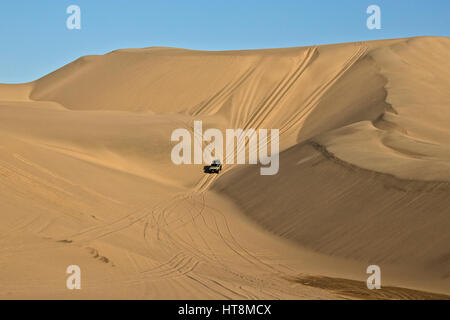 A vehilce driving down the steep slip face of the dunes next to the sea in the Namib Desert Stock Photo