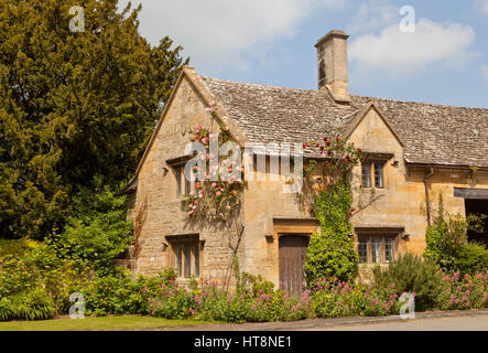 Old stone cottage with pink, red roses, ivy climbing the wall , in English countryside village, on a sunny summer day . Stock Photo