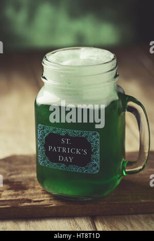 closeup of a mason jar with dyed green beer and the text st. patricks day written in a label attached to it, on a wooden rustic surface Stock Photo