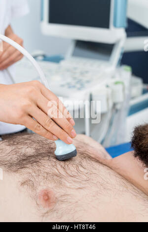 Cropped image of female doctor placing ultrasound probe on male patient's chest in clinic Stock Photo