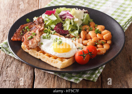 hearty breakfast with fried egg, waffles, bacon, mix salad and beans close-up on the table. horizontal